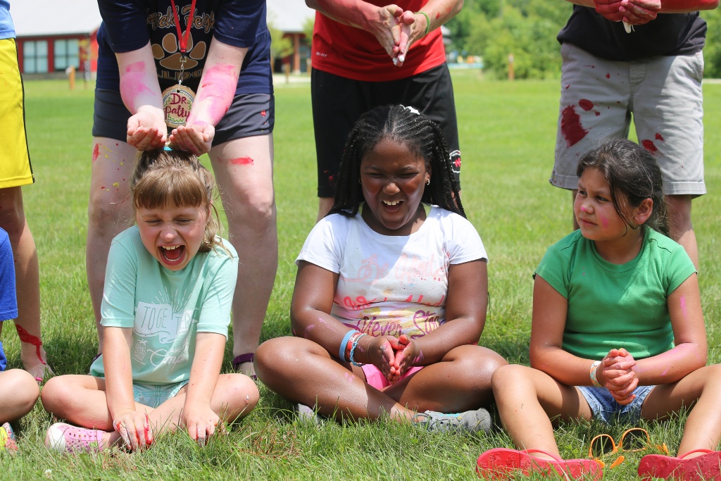 Three campers laughing as Icky Silly supplies are placed on their heads.