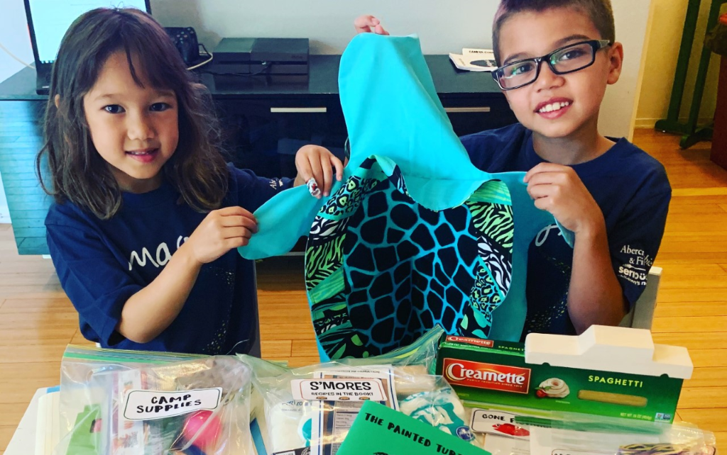 Two sibling campers holding up camp-at-home supplies thanks to The Painted Turtle, the SeriousFun camp in California